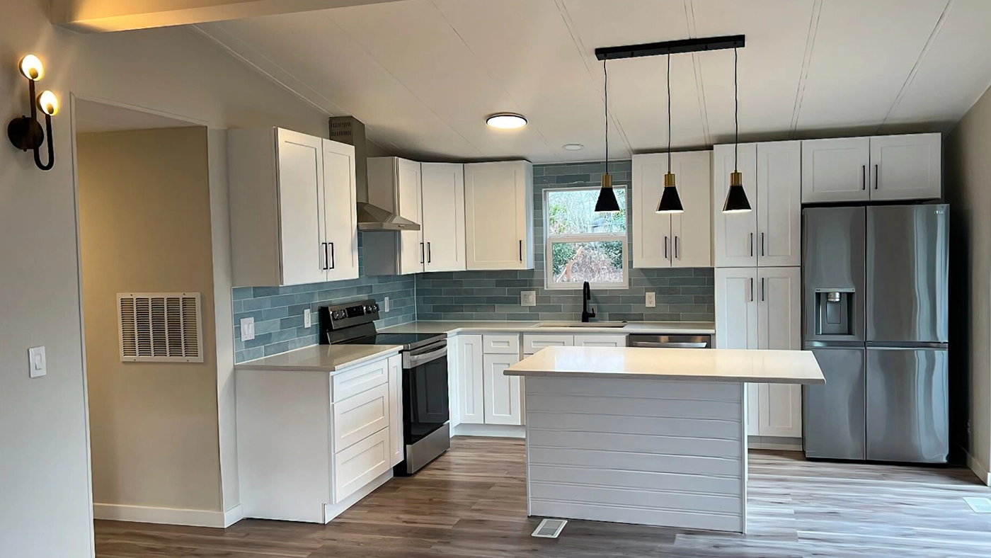 Wide view of the open-concept kitchen at Naakef Seatac Private Home Rental, showcasing a central island, white cabinetry with black hardware, stainless-steel appliances, blue subway tile backsplash, and warm wood-look floors.