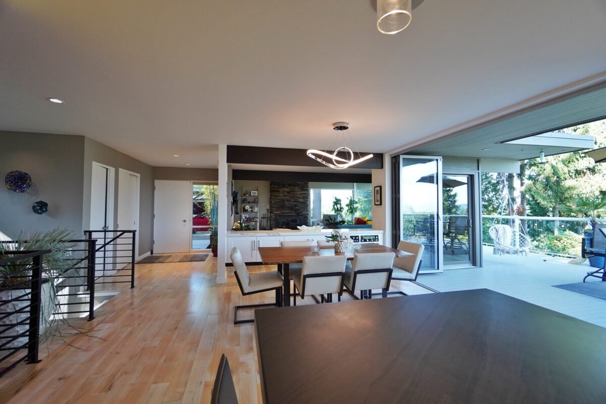 Spacious living room at Naakef Travel Nurse Stay – Lake Forest Park, featuring a curved blue sectional sofa, stone fireplace, and large windows overlooking the greenery.