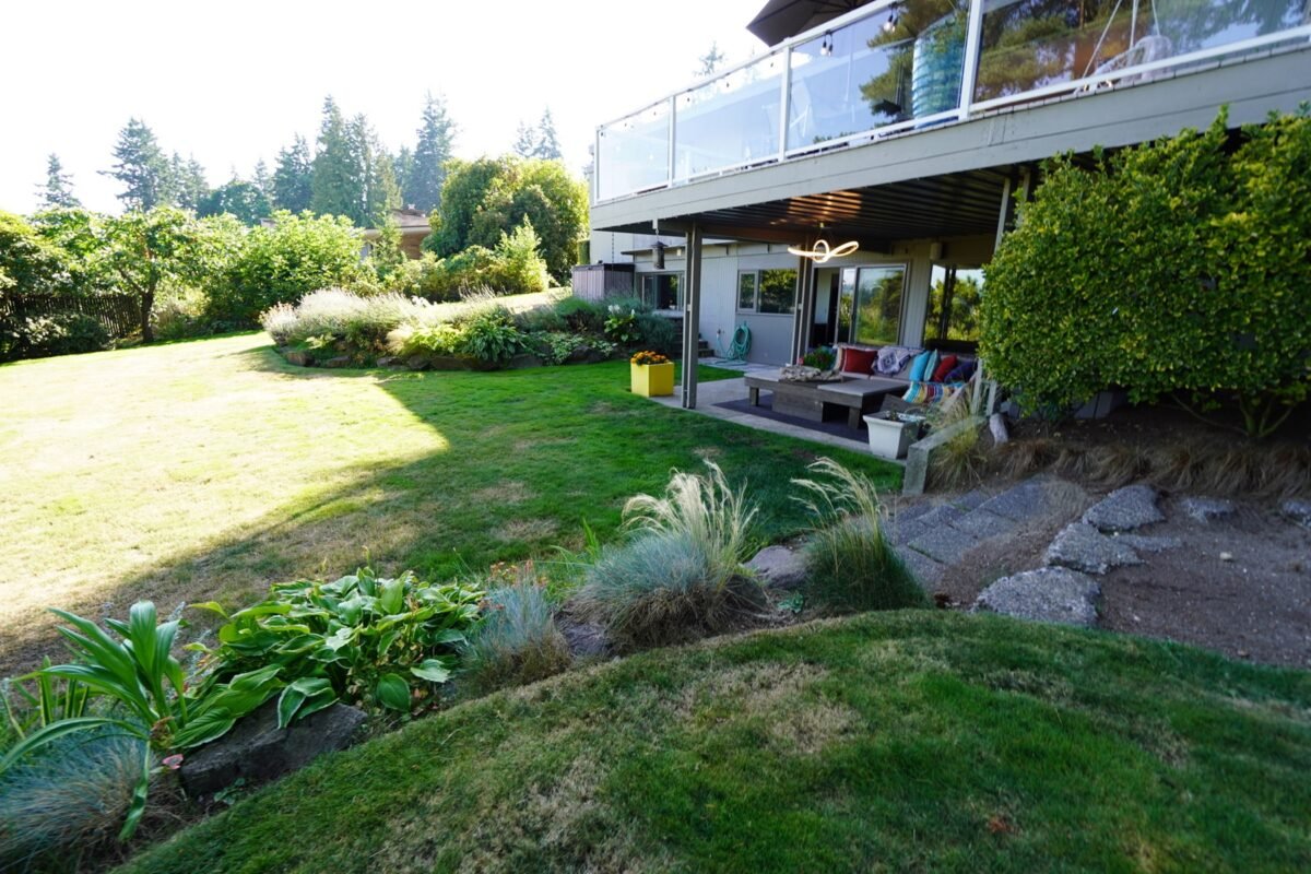 Large grassy backyard with landscaped gardens and patio area at Naakef Travel Nurse Stay – Lake Forest Park.