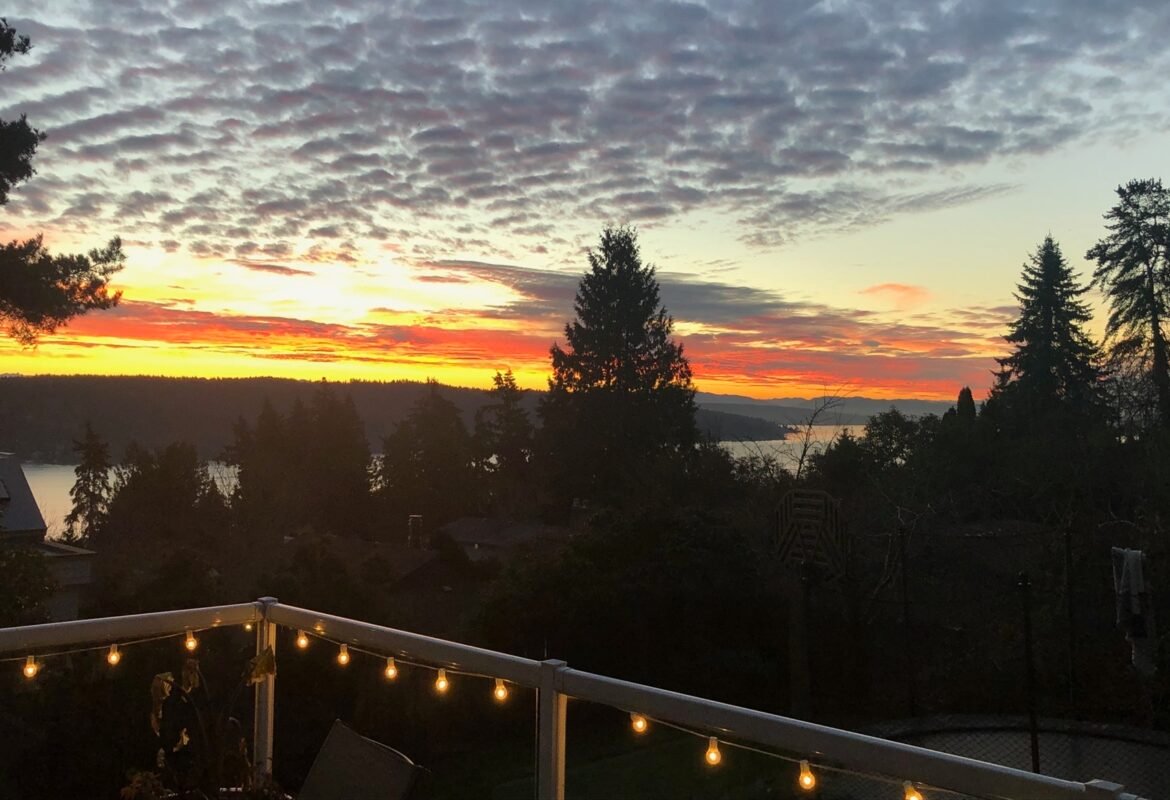 Breathtaking sunset view over the water and trees seen from the private deck of Naakef Travel Nurse Stay – Lake Forest Park.