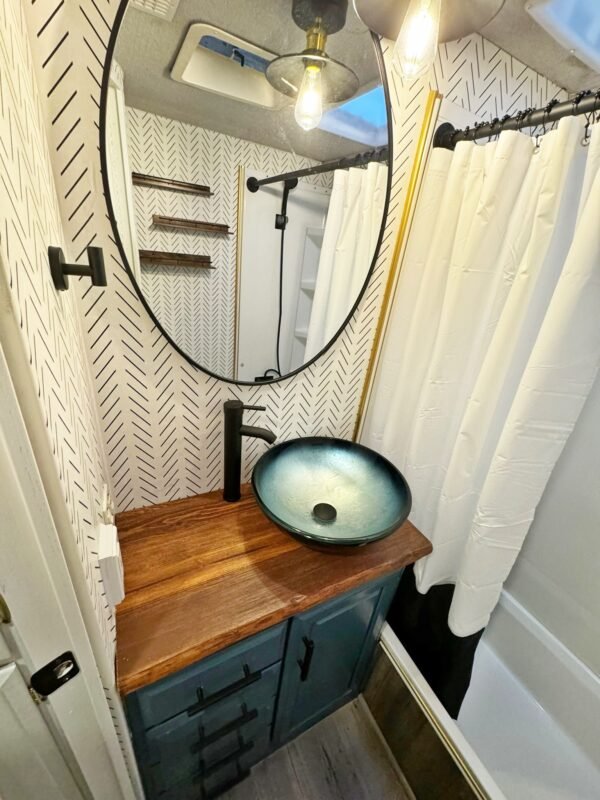 Compact yet functional RV bathroom with a unique vessel sink, patterned wallpaper, and shower stall at Naakef Private Home Rentals – Seatac.