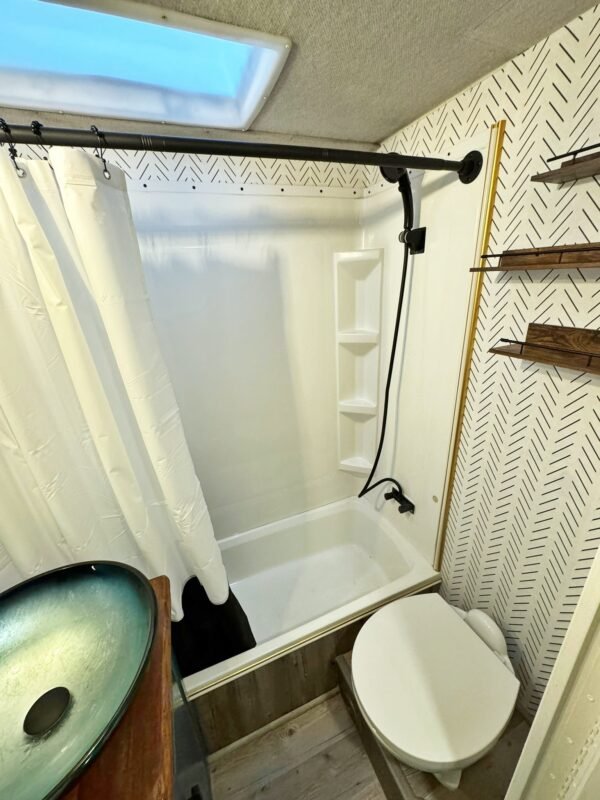 Stylish RV bathroom vanity featuring a blue glass vessel sink, wood countertop, and geometric wallpaper at Naakef Private Home Rentals – Seatac.