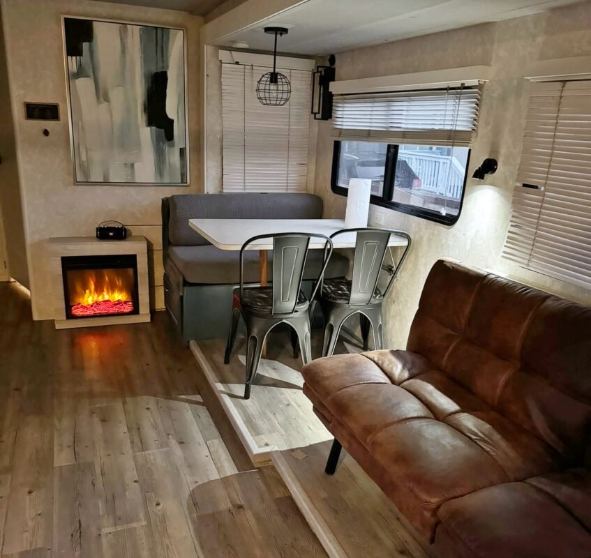 Relaxing RV living room with a brown leather sofa, electric fireplace, and large windows allowing natural light at Naakef Private Home Rentals – Seatac.