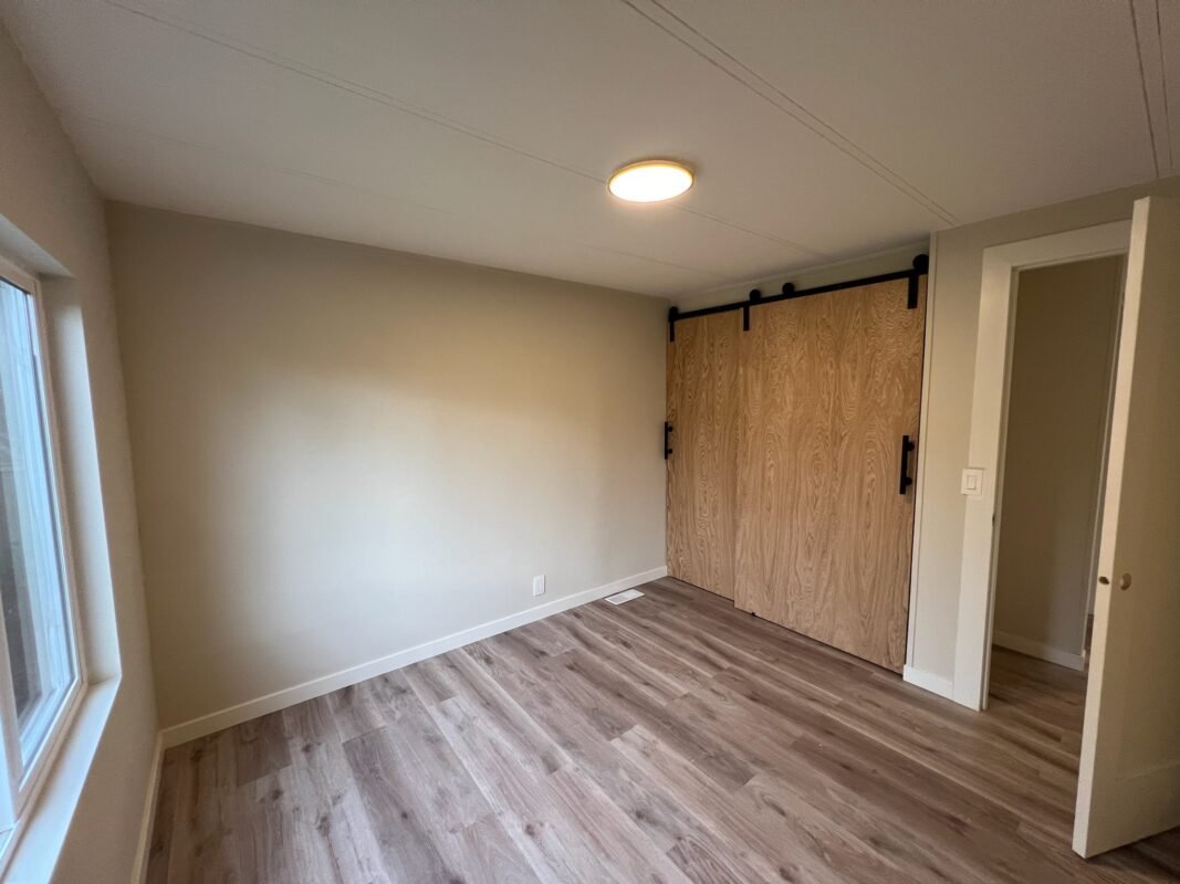 Bright bedroom featuring large windows, wood-look flooring, and a stylish sliding barn door closet at Naakef Private Home Rentals – Seatac.