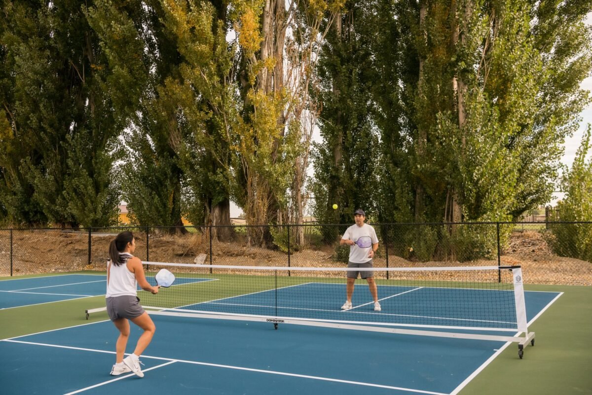 Guests enjoying a game of pickleball on outdoor courts surrounded by tall trees and natural scenery at Sagecliffe Residences by Naakef.
