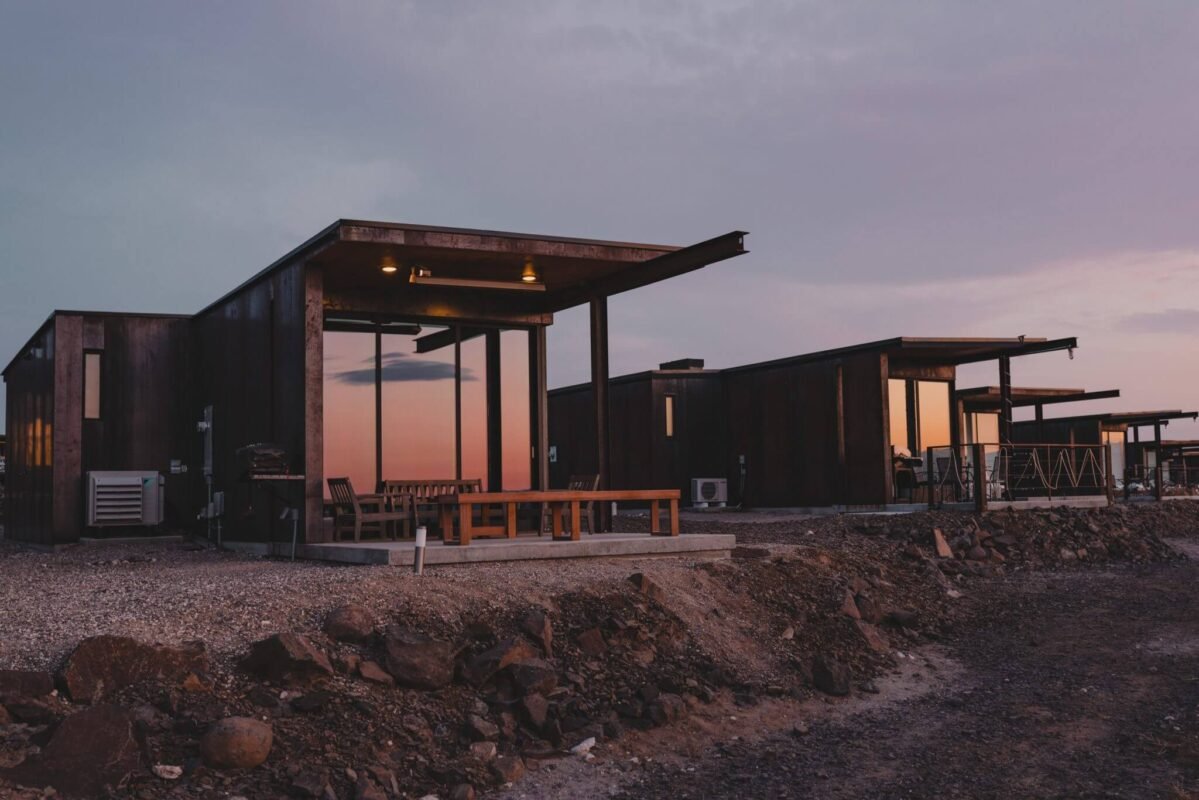 Stylish modern standalone cabins with floor-to-ceiling windows glowing at dusk, set within the rugged landscape of Sagecliffe Residences by Naakef.
