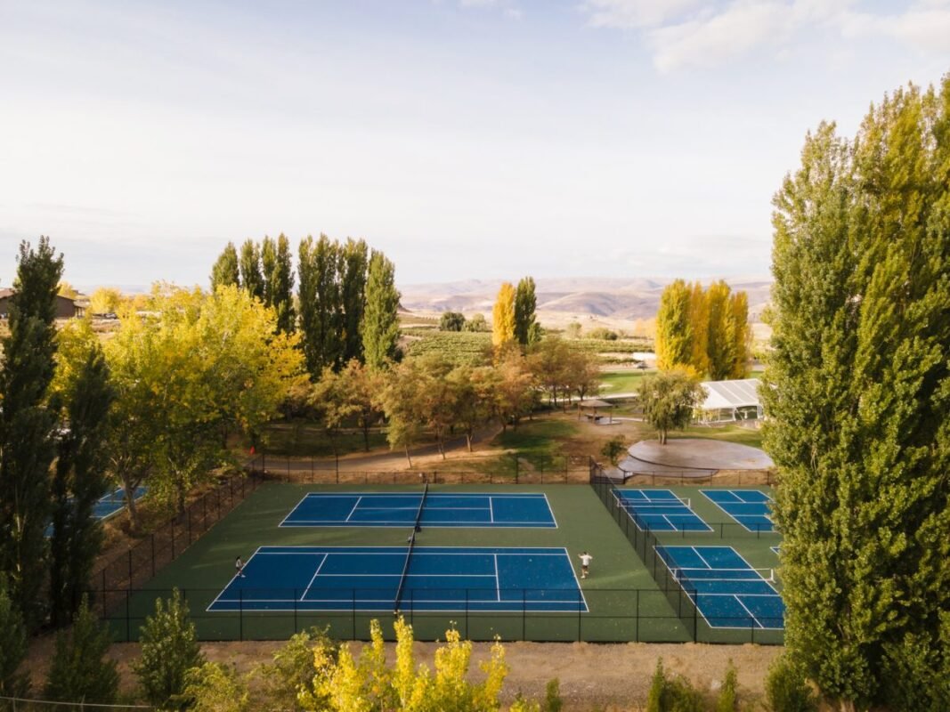 Aerial view of multiple blue and green pickleball and tennis courts nestled among poplar trees with vineyard views at Sagecliffe Residences by Naakef.