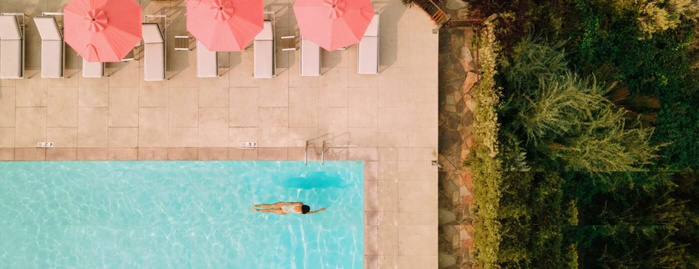 Crystal-clear outdoor swimming pool at Sagecliffe Residences by Naakef with pink umbrellas, lounge chairs, and green landscaping creating a luxurious resort atmosphere.