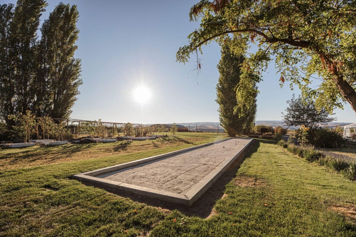 Rustic wooden pergola-covered outdoor lounge area at Sagecliffe Residences by Naakef with comfortable seating and vineyard views beyond native landscaping.