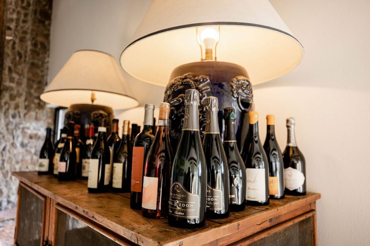 Elegant wine bar display at Sagecliffe Residences by Naakef featuring champagne bottles with ornate neck collars and warm pendant lighting above rustic wooden shelving.