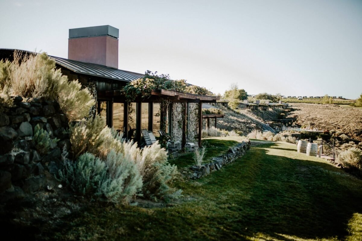Modern stone and metal cabin at Sagecliffe Residences by Naakef nestled in the rolling vineyard landscape with lush green lawns and the Columbia River Gorge in the distance.