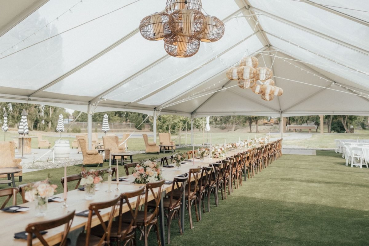 Sophisticated outdoor event tent at Sagecliffe Residences by Naakef featuring long dining tables, hanging woven pendant lights, floral centerpieces, and vineyard views.