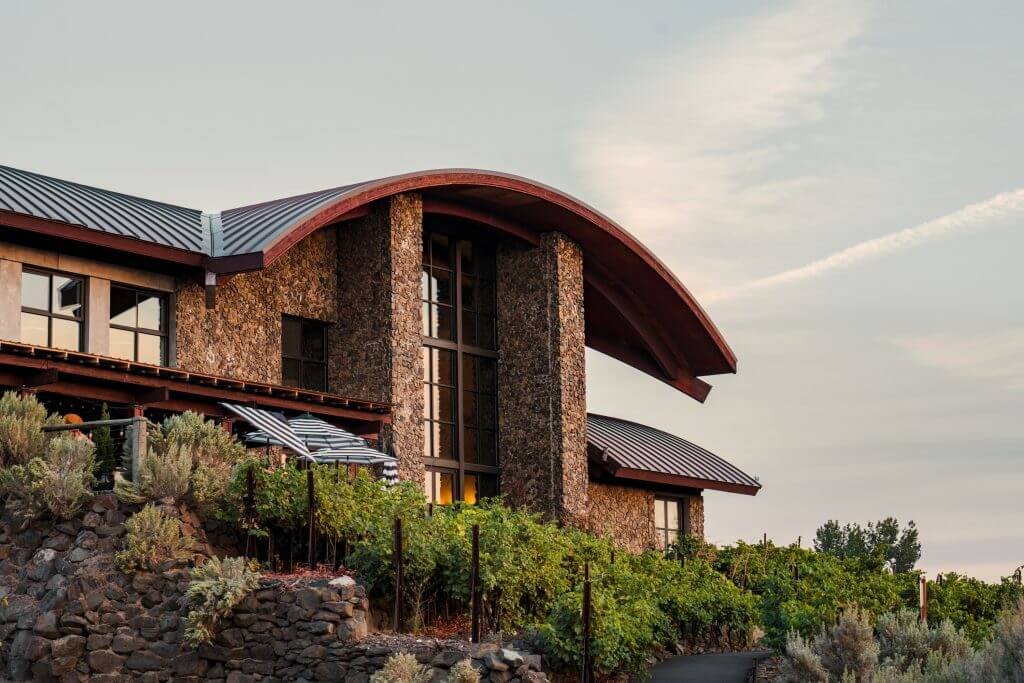 Contemporary stone cabin with distinctive curved metal roof at Sagecliffe Residences by Naakef set among lush vineyards and native landscaping overlooking the gorge.